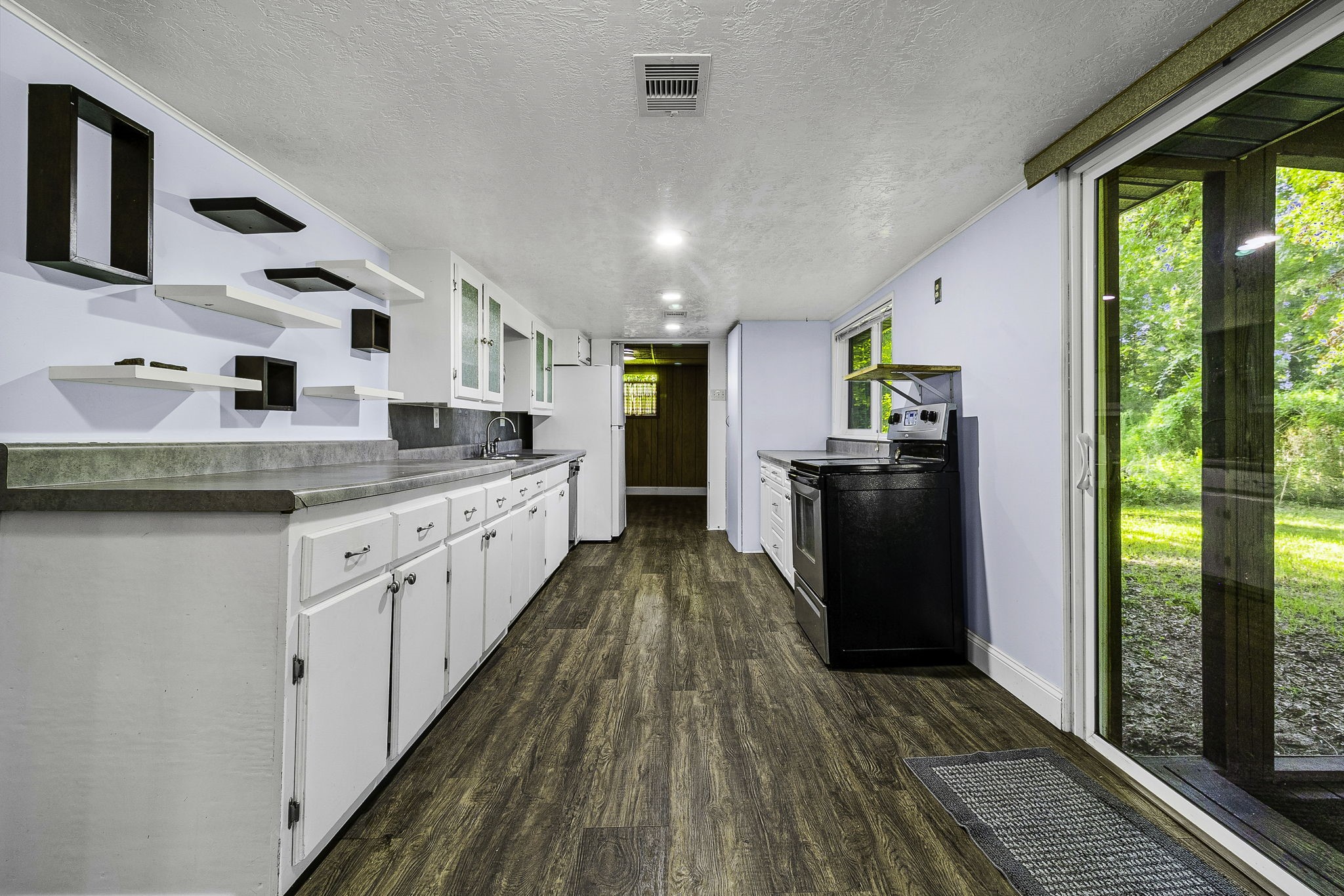 450 River Road Goodrich, TX 77335 - Photo 12 of 40 Spacious galley kitchen featuring modern open shelving, ample countertop space, and sliding glass doors that provide a view of the lush outdoors.