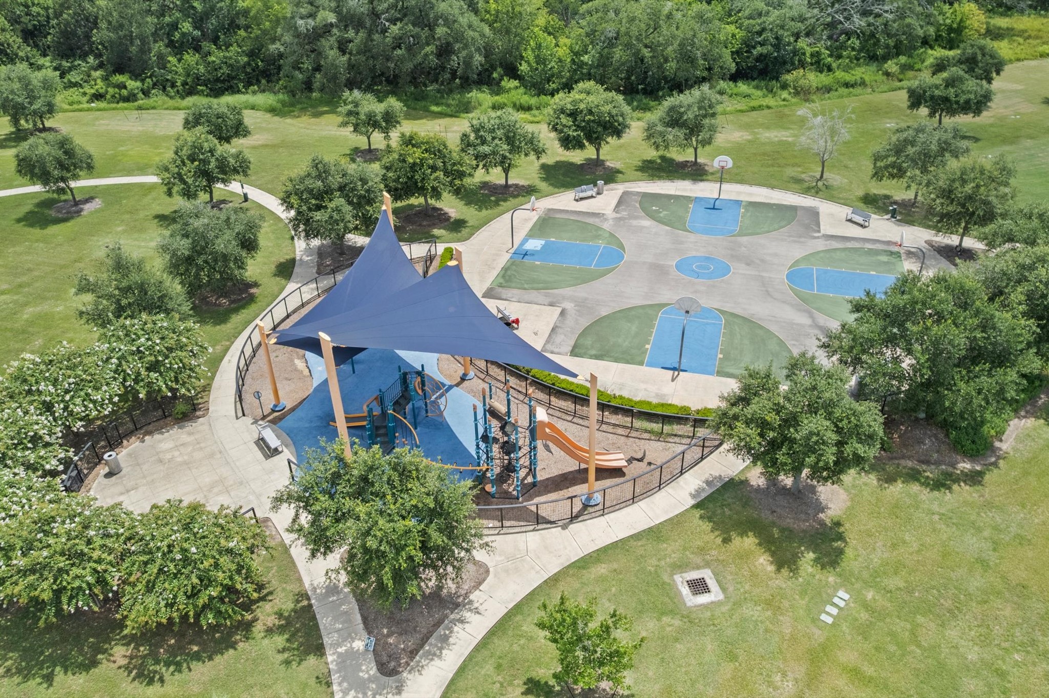 3510 Whitman Drive Rosharon, TX 77583 - Photo 23 of 25 This photo showcases a well-maintained park featuring a modern playground with a shaded area, surrounded by lush greenery. Adjacent to the playground, there's a multi-use sports court ideal for basketball. Perfect for families and outdoor activities.