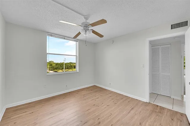 an empty room with wooden floor ceiling fan and windows