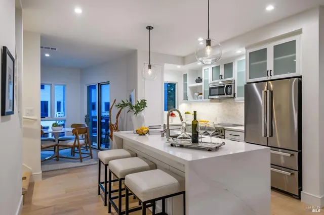 a kitchen with stainless steel appliances granite countertop a refrigerator a sink dishwasher a dining table and chairs with wooden floor