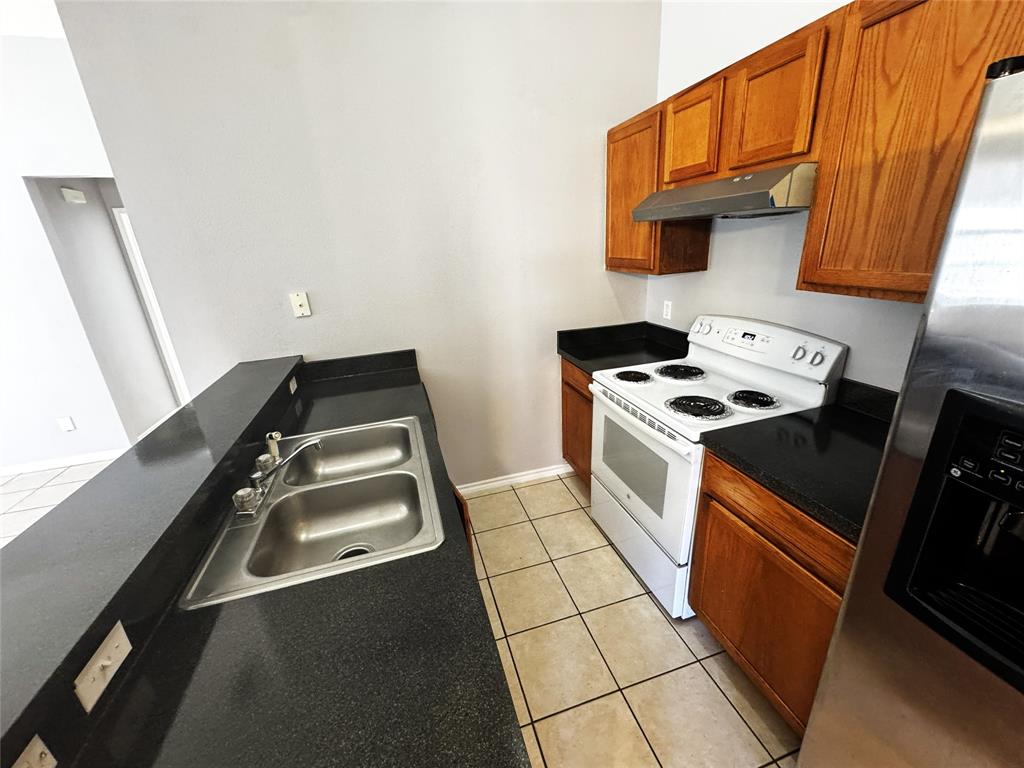 1707 Tina Marie Road, Unit A Arlington, TX 76012 - Photo 23 of 34 Kitchen featuring dark countertops, white electric range, stainless steel fridge, wood finish cabinets, and light tile patterned flooring