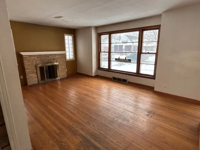 an empty room with wooden floor fireplace and windows