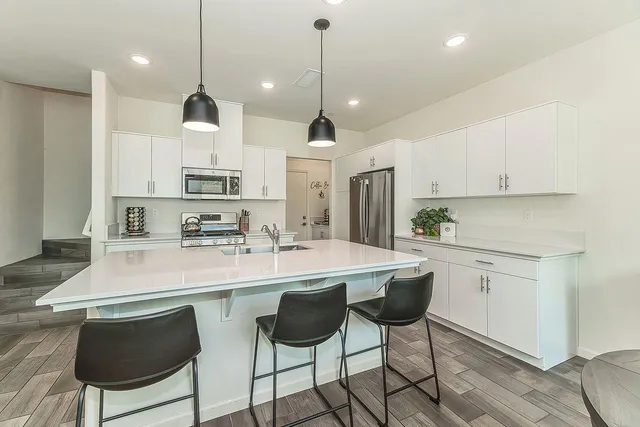 a kitchen with stainless steel appliances granite countertop a sink a stove a refrigerator and white cabinets with wooden floor