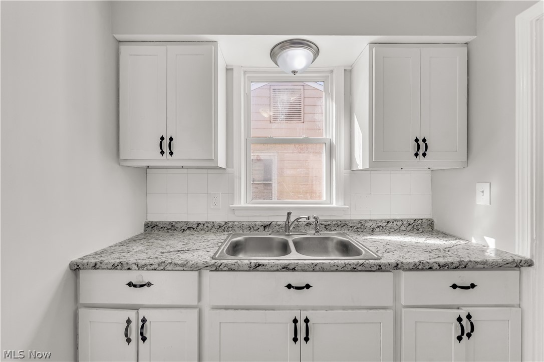 2521 Greenvale Road Cleveland, OH 44121 - Photo 11 of 23 Kitchen area featuring white cabinetry with dark hardware, a double basin stainless steel sink, speckled countertops, and a white tile backsplash