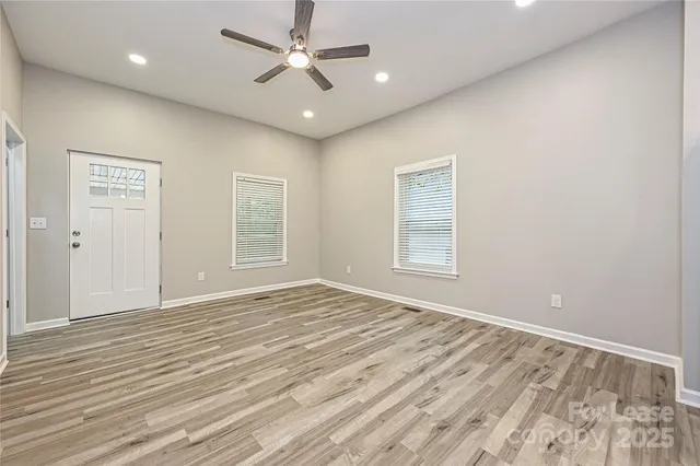 an empty room with wooden floor ceiling fan and windows