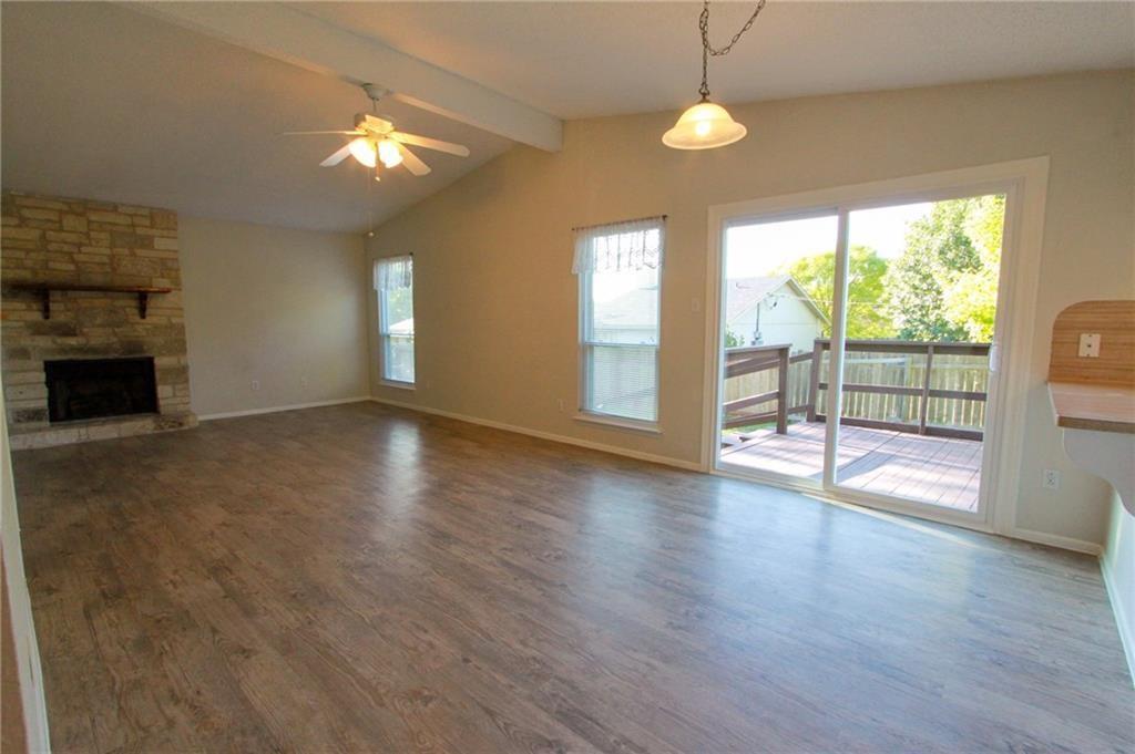 12902 Old San Antonio Road, Unit A Manchaca, TX 78652 - Photo 3 of 9 Spacious living area featuring wood-finish flooring, a stone-front fireplace with a wood mantle, and a vaulted ceiling with a ceiling fan