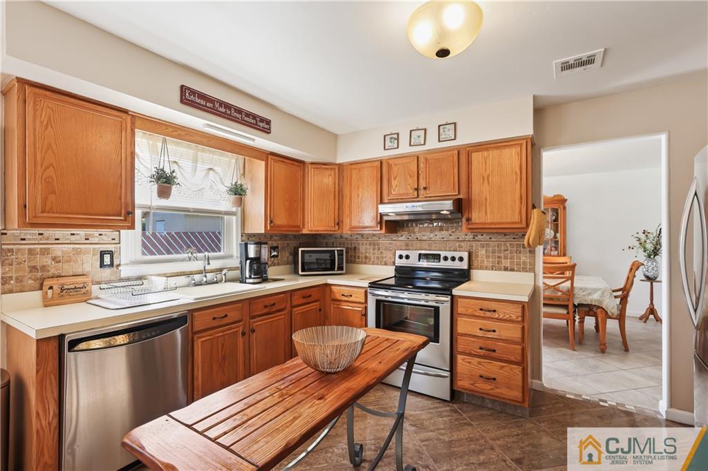 49 South Rhoda Street Monroe Township, NJ 08831 - Photo 3 of 11 a kitchen with stainless steel appliances granite countertop a stove top oven a sink a dining table and chairs with wooden floor