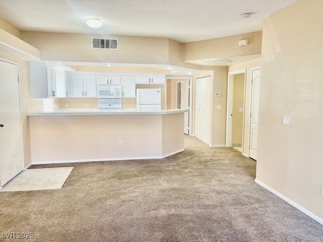 Kitchen with light carpet, white appliances, white cabinetry, and a peninsula