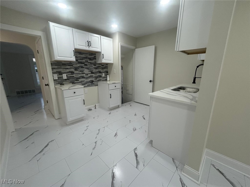 15410 Turney Road Maple Heights, OH 44137 - Photo 13 of 46 Kitchen with tasteful backsplash, white cabinetry, light stone counters, and light marble finish floors