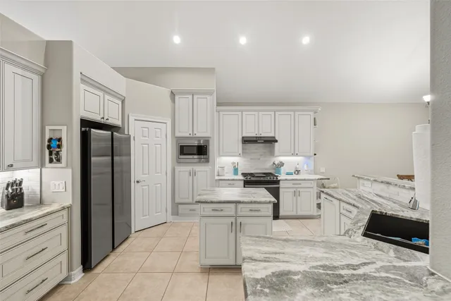 a large kitchen with stainless steel appliances kitchen island granite countertop a refrigerator and a stove top oven