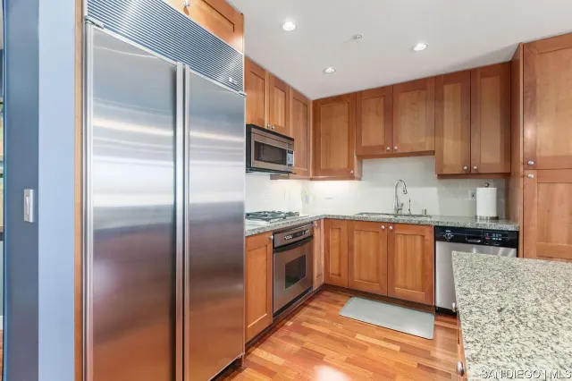 a kitchen with stainless steel appliances granite countertop a refrigerator a stove and a sink with wooden cabinets