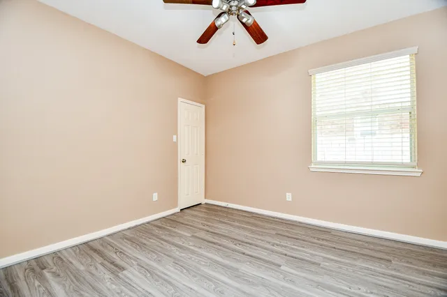 an empty room with wooden floor fan and windows