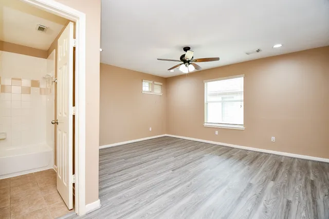 an empty room with wooden floor chandelier fan and windows