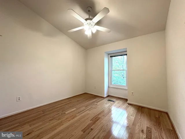 an empty room with wooden floor fan and windows