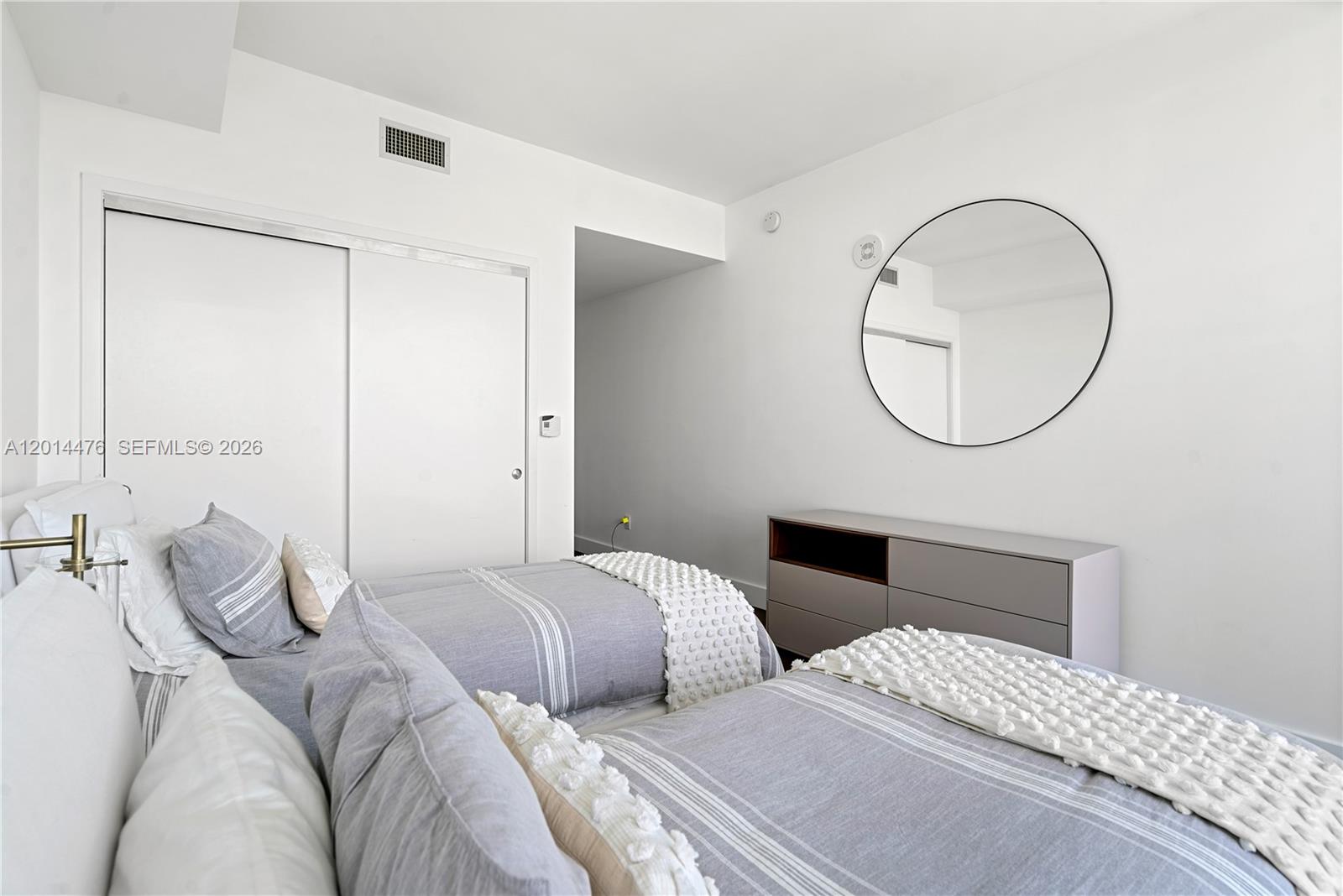 360 Ocean Drive, Unit 1106S Key Biscayne, FL 33149 - Photo 15 of 67 Guest Bedroom – A clean, modern bedroom layout includes a sleek dresser, round wall mirror, and soft neutral bedding. Sliding closet doors and simple finishes keep the space polished and efficient.