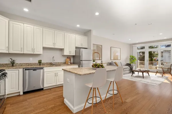 a kitchen with stainless steel appliances granite countertop a stove top oven a sink a refrigerator and white cabinets with wooden floor