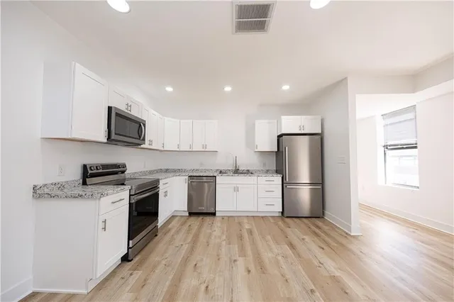 a large kitchen with kitchen island a stove a sink dishwasher a refrigerator and white cabinets with wooden floor