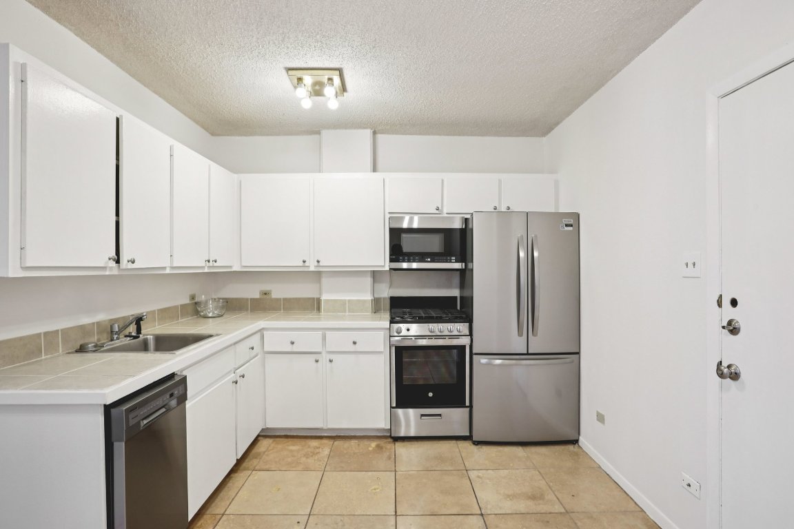 1212 Guadalupe Street, Unit 210 Austin, TX 78701 - Photo 7 of 12 Kitchen with appliances with stainless steel finishes, white cabinets, a textured ceiling, tile countertops, and light tile patterned flooring