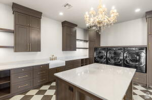 1141 East Lost Ridge Drive Washington, UT 84780 - Photo 56 of 108 Dedicated laundry room featuring an overhead crystal chandelier, checkerboard flooring, a deep basin sink, extensive cabinetry, and a central island with a solid surface countertop