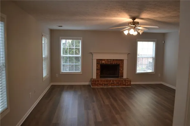 a view of an empty room with wooden floor fireplace and a window