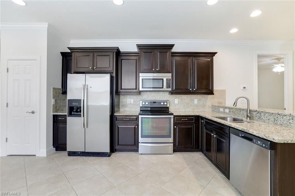 13366 Kent Street Naples, FL 34109 - Photo 5 of 23 Kitchen with stainless steel appliances, crown molding, decorative backsplash, dark brown cabinetry, and recessed lighting