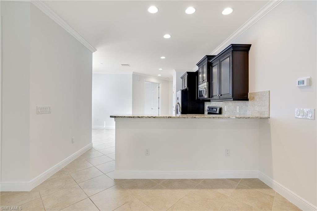 13366 Kent Street Naples, FL 34109 - Photo 9 of 23 Kitchen featuring ornamental molding, light stone counters, backsplash, dark cabinets, and light tile patterned flooring