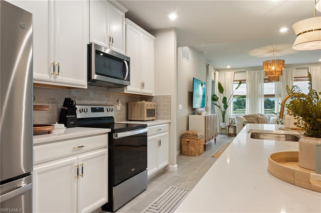 4638 Arboretum Circle, Unit 102 Naples, FL 34112 - Photo 13 of 20 a kitchen with stainless steel appliances granite countertop a refrigerator a stove top oven a sink dishwasher and white cabinets with wooden floor