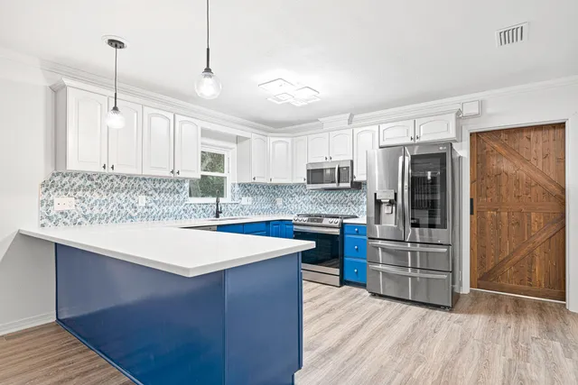 a kitchen with stainless steel appliances kitchen island granite countertop a refrigerator a stove a sink and white cabinets with wooden floor