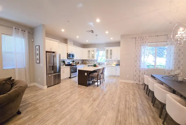 a kitchen with stainless steel appliances kitchen island granite countertop a refrigerator oven a sink dishwasher and white cabinets with wooden floor