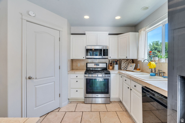 1727 South Sandhill Road Orem, UT 84058 - Photo 9 of 27 Kitchen featuring white cabinetry, stainless steel range and microwave, tile flooring, and a window above the sink