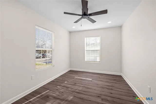 an empty room with wooden floor ceiling fan and windows