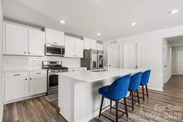 a kitchen with stainless steel appliances a sink a stove a refrigerator cabinets and a dining table with wooden floor