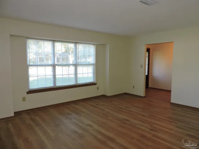 a view of an empty room with wooden floor and a window