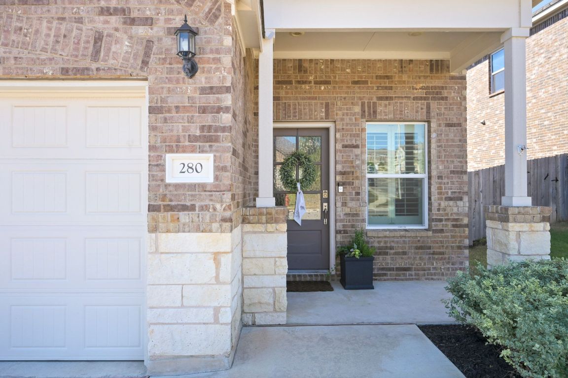 Doorway to property with covered porch, brick siding, and a garage