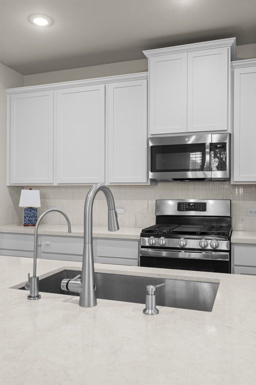 280 Pepperbark Loop Buda, TX 78610 - Photo 11 of 38 Kitchen featuring stainless steel appliances, white cabinetry, light stone counters, and recessed lighting