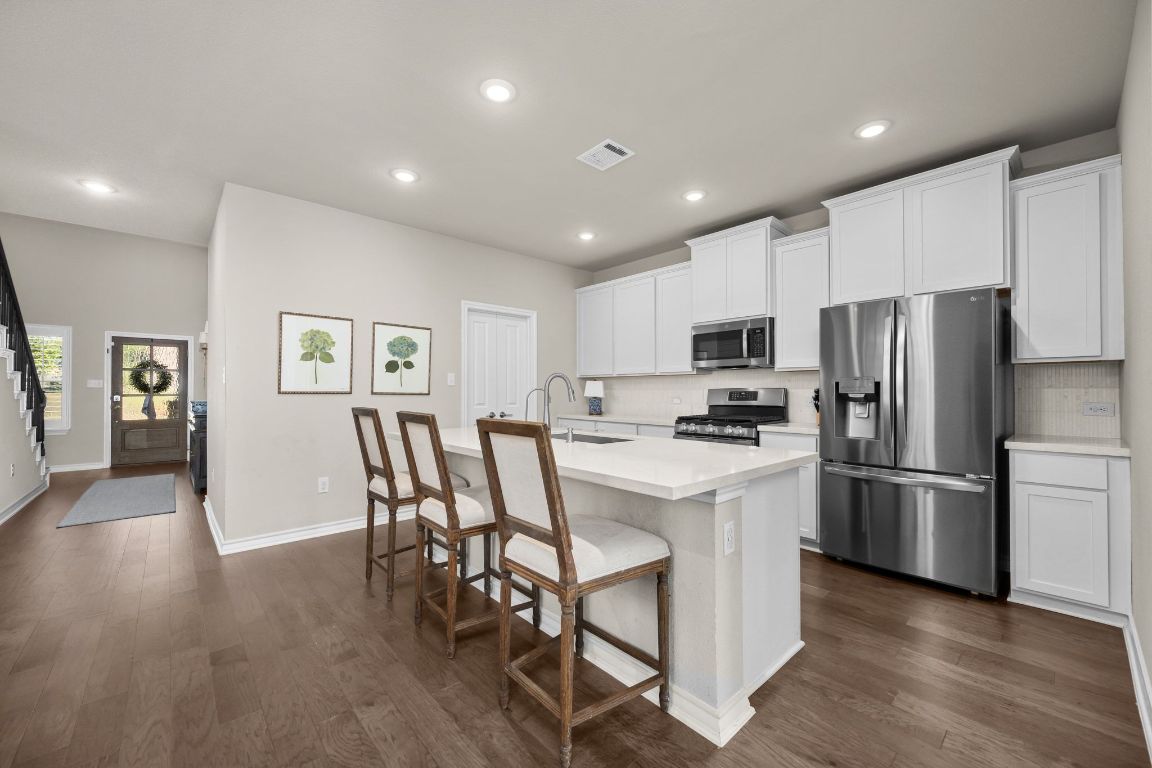 280 Pepperbark Loop Buda, TX 78610 - Photo 12 of 38 Kitchen featuring appliances with stainless steel finishes, an island with sink, a kitchen breakfast bar, white cabinetry, and decorative backsplash