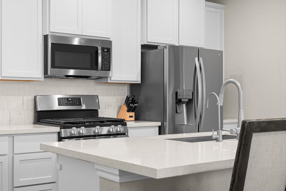 280 Pepperbark Loop Buda, TX 78610 - Photo 13 of 38 Kitchen featuring appliances with stainless steel finishes, light stone counters, white cabinetry, and decorative backsplash