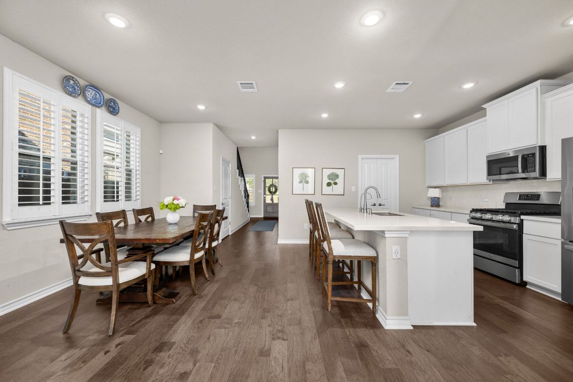 280 Pepperbark Loop Buda, TX 78610 - Photo 14 of 38 Kitchen with appliances with stainless steel finishes, white cabinetry, a center island with sink, dark wood-style floors, and a breakfast bar
