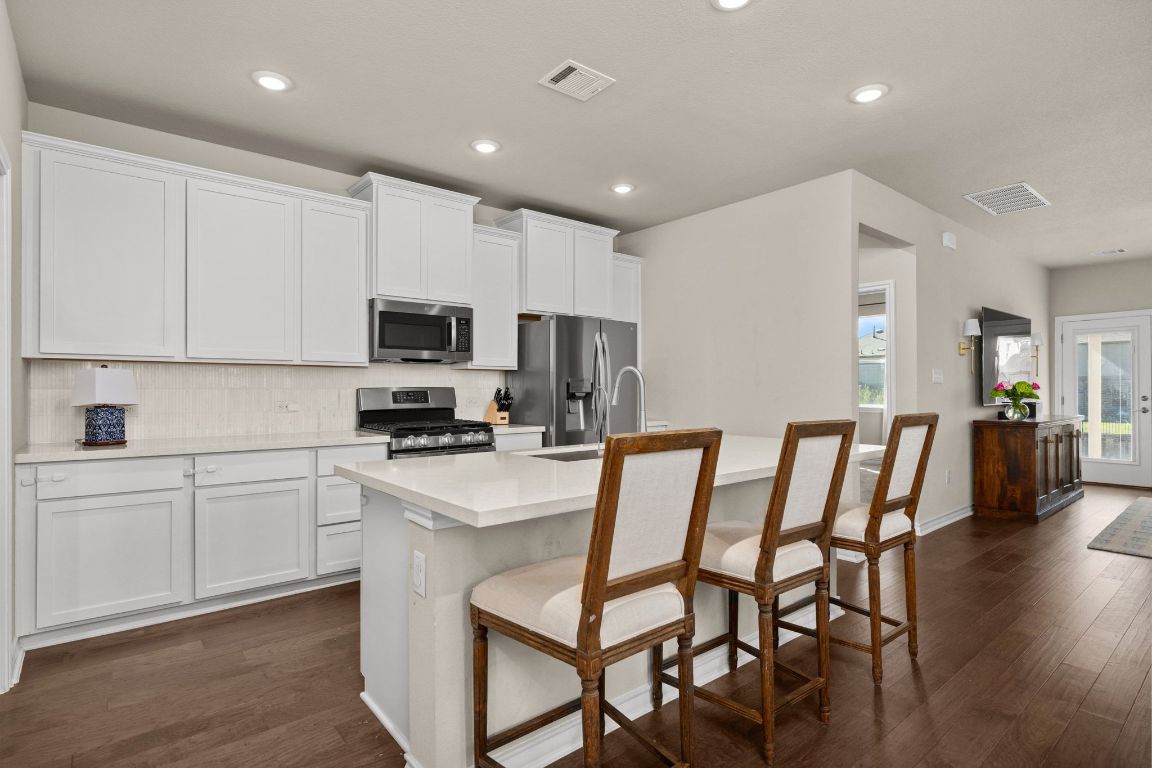 280 Pepperbark Loop Buda, TX 78610 - Photo 9 of 38 Kitchen with a breakfast bar, white cabinetry, backsplash, stainless steel appliances, and recessed lighting