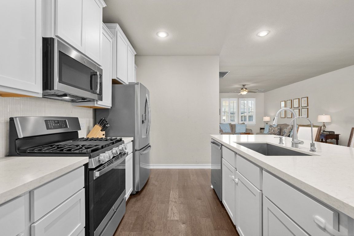 280 Pepperbark Loop Buda, TX 78610 - Photo 10 of 38 Kitchen featuring stainless steel appliances, white cabinets, dark wood-type flooring, light stone counters, and recessed lighting