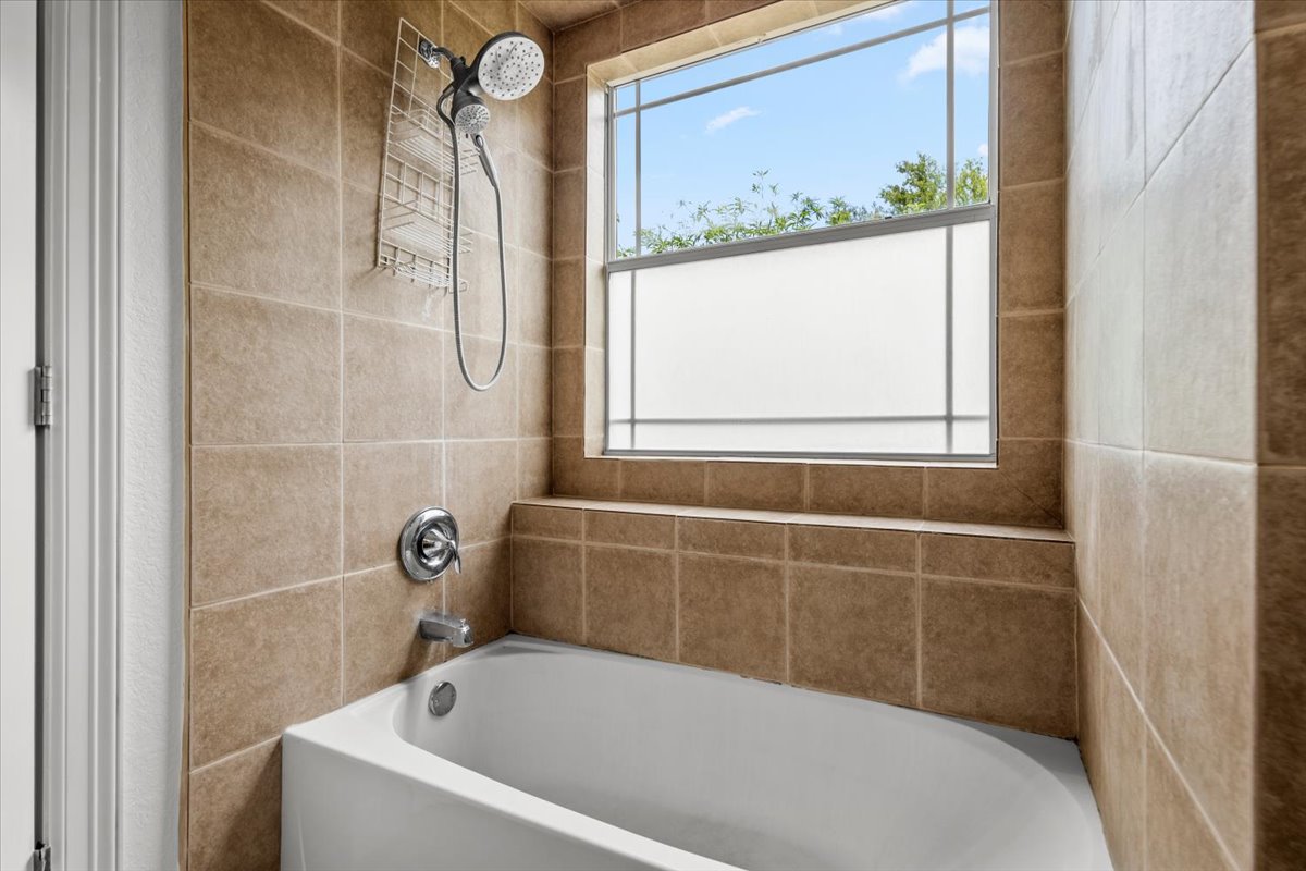 437 Balch Road Elgin, TX 78621 - Photo 16 of 37 A well-appointed bathroom with a spacious tub and tiled surround, offering natural light through a generous window.