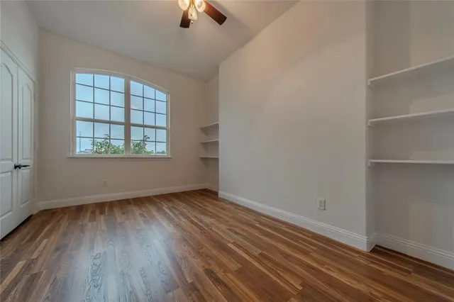 an empty room with wooden floor chandelier fan and windows