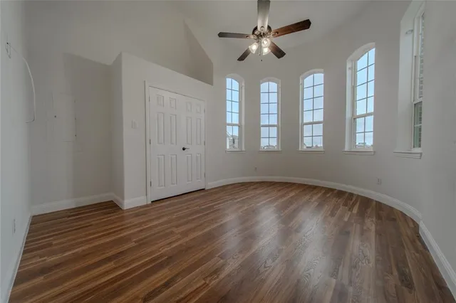 an empty room with wooden floor chandelier fan and windows