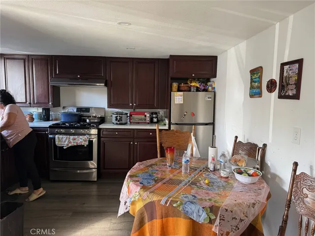 a kitchen with stainless steel appliances kitchen island granite countertop a refrigerator a stove a sink dishwasher and a dining table with wooden floor