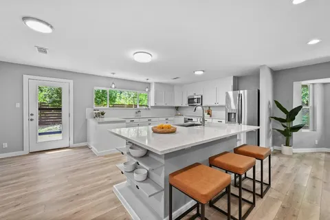 a kitchen with stainless steel appliances kitchen island granite countertop a dining table chairs and a refrigerator