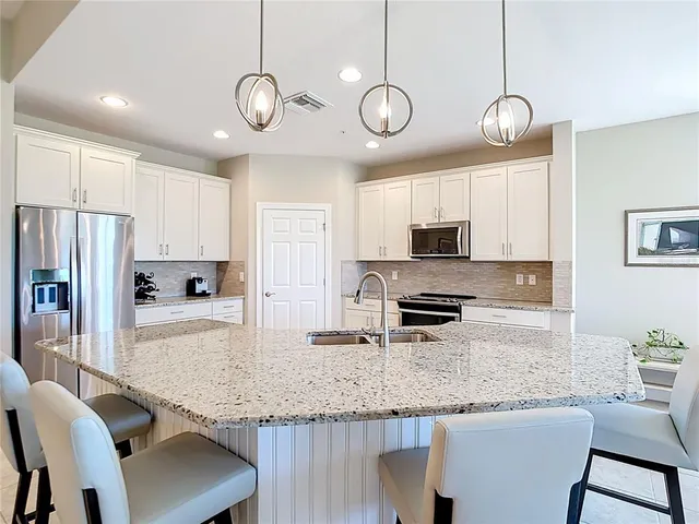 a kitchen with stainless steel appliances granite countertop a sink a stove a refrigerator a dining table and chairs with wooden floor