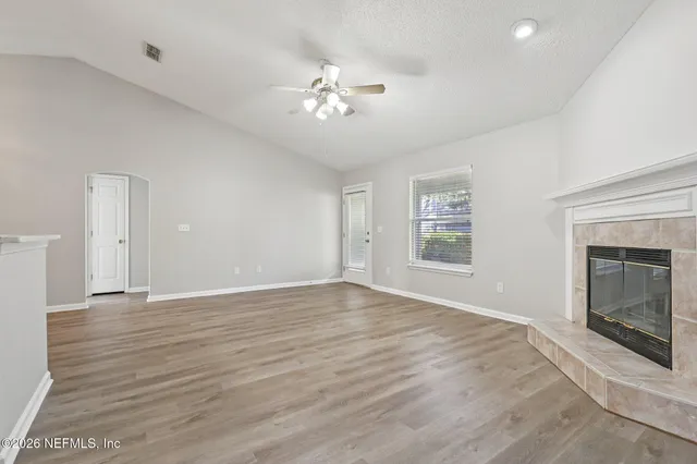 a view of an empty room with wooden floor fireplace and a window