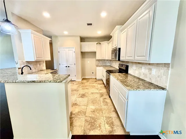 a large kitchen with kitchen island granite countertop a sink and white cabinets