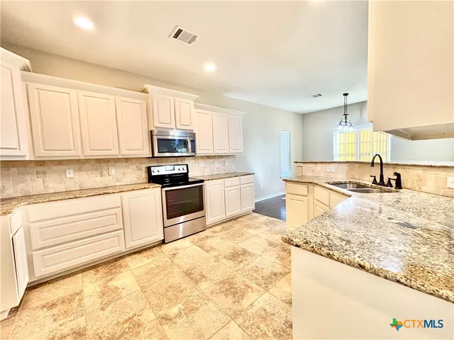 a kitchen with granite countertop white cabinets and stainless steel appliances