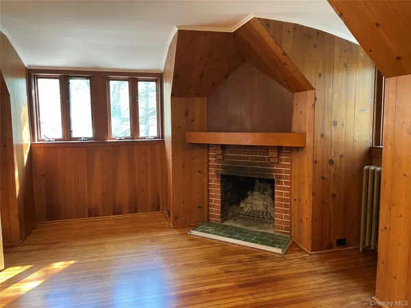 a view of an empty room with wooden floor fireplace and a window